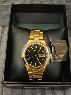 Seiko SGF792 Gold Plated – Black Dial – Full Set – near mint Condition - Säljer en stilren Seiko SGF792 i nyskick (mint condition). Klassisk dressklocka med tidlös design. Ca 36-37mm boett Gold plated Black dial Quickset day-date Quartz (7N43-9070) Nytt batteri – redo att användas direkt   Full set: original box, garantikort, manual + tag  Skyddsplast kvar på glaset Serienummer: 172380 (tillverkad juli 2001 enligt Seiko serial) Klockan är ca 25 år gammal men i väldigt fint skick – perfekt både till vardag och samling.