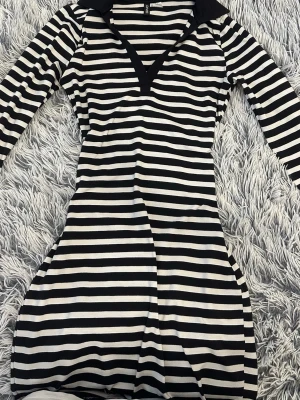 Randig svartvit långärmad mini klänning - Säljer en svartvit randig klänning med lång ärm och v-ringad hals. Klänningen har en figurnära snatched passform och är i mjukt stretchigt material som formar kroppen fint.