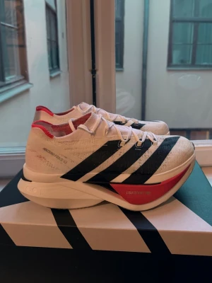 Adidas Adizero Prime X3 sneakers - Adidas Adizero Prime X3 sneakers i vitt med svarta ränder och röda detaljer. Ovandelen är i lätt meshmaterial och sulan är extra hög och chunky med röda och svarta inslag. Snygg sportig look och tydlig Adidas-branding på sidan.