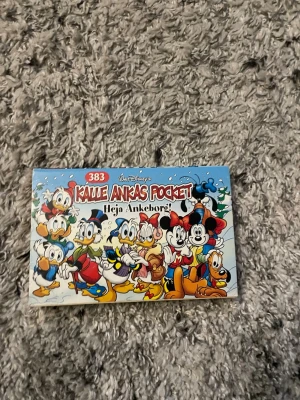 Kalle Ankas Pocket 383 Heja Ankeborg - Kalle Ankas Pocket nummer 383, 'Heja Ankeborg!', är en färgglad pocketbok med klassiska Disney-karaktärer som Kalle Anka, Musse Pigg och Långben på omslaget. Boken har ett vintertema med snö och tecknade figurer i vinterkläder.