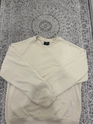 Beige loose fit sweatshirt från H&M - En stilren beige sweatshirt från H&M i loose fit-modell. Tröjan har rund halsringning, långa ärmar och ribbade muddar vid ärmslut och nederkant. Perfekt för en avslappnad och trendig look.