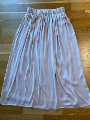 Ljusrosa långkjol med satinkänsla - Kjolen har ett mjukt, glansigt tyg som faller snyggt och ger en elegant look. Underkjol finns. Perfekt för dig som gillar en enkel men stilren stil.Längd 76 cm.