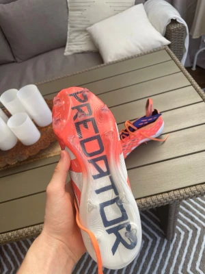 Adidas Predator orange fotbollsskor - Säljer ett par Adidas Predator elite fotbollsskor i en riktigt snygg orange färg med vita detaljer och svarta inslag. Skorna har snörning, låg vikt och mönstrad ovansida för bättre bollkontroll. Sulan har dobbar för spel på gräs men funkar även väldigt bra på konstgräs. (Påse kommer med) 