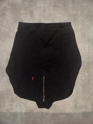 Svarta cykelbyxor med dragkedja Rapha - Svarta cykelbyxor från Rapha med röd broderad logga på framsidan och dragkedja. Tight passform och tillverkade i stretchigt syntetmaterial, designade för cykling och sport.