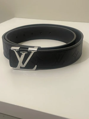 Svart L V bälte - Snyggt  skärp från   i skinn med klassisk i  på spännet. Bältet har präglade monogramdetaljer längs hela remmen och en stilren, modern look. Perfekt accessoar för att lyfta vilken outfit som helst.