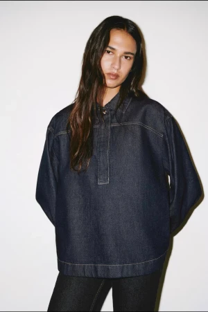 Mörkblå denim henley från ARKET - Säljer en mörkblå henley-skjorta i denim från ARKET. Skjortan har lång ärm, klassisk krage och knappdetalj framtill. Oversized passform och tillverkad i bomull. Perfekt för en avslappnad och trendig look.
