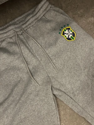 Grå Brasilien hoodie med tryck - Skit snygg Brazil tracksuit som jag råkat köpa fel storlek av! Tracksuiten är 100% äkta och köpt för 1200kr dom orginal pris. Priset kan även diskuteras. S-M är storleken.