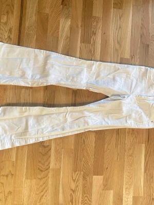 Vita bootcut jeans - Säljer ett par vita bootcut jeans med klassisk femficksdesign. Jeansen har smal passform och är tillverkade i ett stretchigt material som sitter snyggt. 