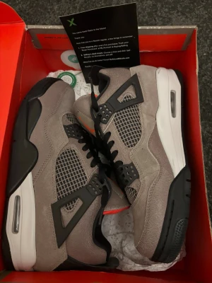 Air Jordan 4 Taupe Haze sneakers - Grymma Air Jordan 4 Taupe Haze med mocka i taupegrått, svarta detaljer och vit mellansula. Klassisk siluett med meshpaneler och ikoniska plastvingar. Röd insida för extra kontrast. Perfekta för dig som vill sticka ut med stilrena sneakers. Storlek 43 och helt oanvända. Hör gärna av dig om du har några funderingar.