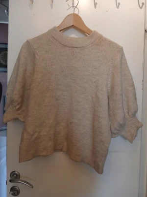Beige stickad tröja från Vila - Beige stickad tröja från Vila med korta puffärmar och ribbad halsringning. Tröjan har en avslappnad passform och är perfekt för lager-på-lager. Mjuk och skön, passar till många olika outfits.
