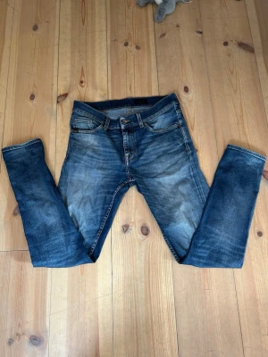 Blå slim fit jeans med slitningar - Snygga blå slim fit jeans med lätt slitna detaljer och klassisk femficksdesign. Jeansen har en medelhög midja och smal passform hela vägen ner. Perfekta för en avslappnad och trendig look.
