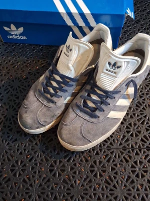 Blå Adidas Gazelle skor - Blå Adidas Gazelle skor, storlek 42. Looselacade Helt okej skick. Mockan är lite uppborstad och sulan och flärpen är lite leriga. Annars är dem i bra skick. Lådan följer även med. Hör av dig om du har frågor eller om du vill diskutera priset.