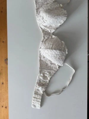 Vit spets-bh med blommönster - Säljer en vit bh med vackert blommönstrad spets. Bh:n har justerbara axelband och hakknäppning bak. Materialet är mjukt och spetsen ger en romantisk känsla. Perfekt för dig som gillar feminina detaljer.