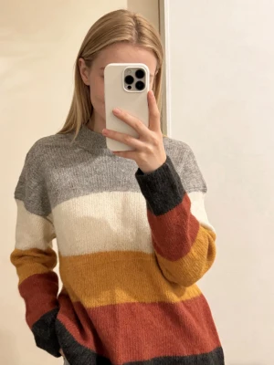 Randig stickad wool tröja från Lindex - 35%wool and 30% mohair. Mysig stickad tröja från Lindex med breda ränder i grått, vitt, gult och rostrött. Tröjan har en avslappnad passform, rund halsringning och långa ärmar. Perfekt för dig som gillar färg och vill ha en skön vardagslook.