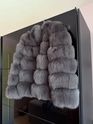 Grå fluffig pälsjacka(äkta pälsjacka) - Säljer en supermjuk och fluffig grå pälsjacka med breda, quiltade sektioner. Jackan har en kortare modell och rundad krage som ger en trendig look. Perfekt för dig som vill sticka ut och hålla dig varm under vintern.