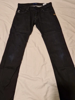 Svarta jeans från G-Star RAW - Tjena, säljer ett par Snygga svarta jeans från G-Star RAW med raka ben och klassisk femficksdesign. Jeansen har diskreta logodetaljer både fram och bak samt kontrastsömmar. Tillverkade i slitstarkt denimtyg som ger en cool och tidlös look Storlek 31, och storlek 32 i längd, Tveka inte att skriva vid några funderingar.