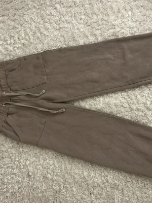 Beige mjukisbyxor med raka ben - Säljer ett par beige mjukisbyxor med raka ben och resår i midjan. Byxorna har dragsko och stora fickor både fram och bak. Tillverkade i mjukt och skönt material, perfekta för chill dagar. Passar dig som gillar en avslappnad och enkel stil.