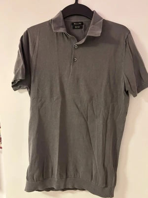Grå pikétröja Massimo Dutti - Klassisk grå pikétröja från Massimo Dutti med korta ärmar och krage. Tröjan har två knappar framtill och är tillverkad i mjuk bomull som känns skön mot huden. Perfekt till jeans eller chinos för en clean look. Funkar för alla aktiviteter, golf m.m.