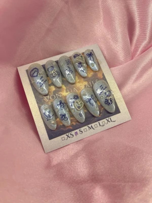 BlueBell (S);Medium Almond - Snygga handgjorda press-on naglar i silverglittrig bas med blå motiv som rosetter, hjärtan, björnar och stjärnor. Naglarna har en medium almondform och är dekorerade med detaljerade illustrationer för en unik look. Perfekt för dig som vill sticka ut med dina naglar. S: 15 mm, 11,5 mm, 12 mm, 11 mm, 9 mm 