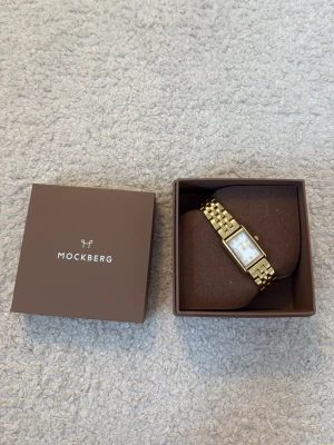 Guldfärgad klocka från Mockberg - Snygg guldfärgad klocka från Mockberg med rektangulär urtavla och länkarmband. Urtavlan är vit med guldiga detaljer och stilrena markeringar. Kommer i originalask, perfekt för dig som gillar klassisk och elegant stil. Regular Timeless är namnet 🌸🌸