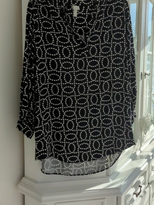 Svart blus med mönster från H&M - Svart blus från H&M med vitt cirkelmönster som liknar pärlor. Blusen har trekvartsärm och en lös, avslappnad passform. Tillverkad i ett lätt och luftigt material som känns skönt mot huden. Perfekt för dig som gillar grafiska mönster och stilren design. Är storlek S men passar upp till XXL