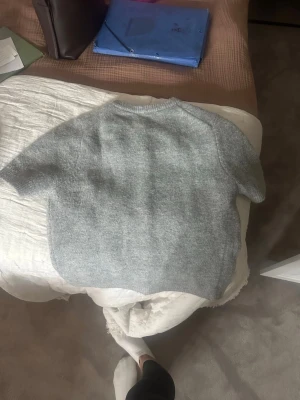 Grå kortärmad kofta från Zara - Mysig grå kofta från Zara med korta ärmar och rund halsringning. Koftan har knappar framtill och är gjord i ett mjukt, stickat material som känns fluffigt. Perfekt för lager på lager och enkel att matcha med olika outfits.