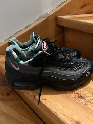 Nike Air Max 95 x Corteiz svart/grå - Unika Nike Air Max 95 x Corteiz sneakers i svart och grått med rosa detaljer. Skorna har mesh och läderpaneler, samt camomönstrat innerfoder. Swoosh och Corteiz-logga i rosa brodyr. Tjock sula med synlig Air-enhet för extra komfort.
