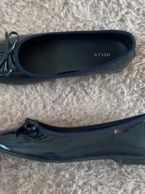 Mörkblå lackballerinaskor från Nelly - Snygga mörkblå ballerinaskor från Nelly i glansigt lackmaterial. De är helt oanvända, därav inga defekter! I storlek 38!