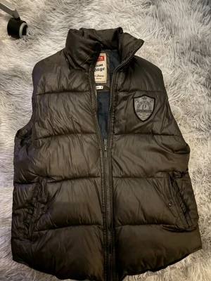 Svart dunväst från Jack & Jones - Snygg svart dunväst från Jack & Jones med hög krage och dragkedja framtill. Är självklart öppen för prisförslag och säljer fler varor så köper du många får du också mängdrabatt. Obs säljes som på bild.