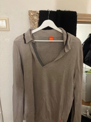 Beige stickad tröja från Hugo Boss - Snygg beige stickad tröja från Hugo Boss med unik krage och diskreta mörka detaljer. Tröjan har lång ärm och är tillverkad i ett tunt, mjukt material som passar perfekt för lager på lager. Klassisk och stilren design, tröjan går att använda både för tjejer och killar och går att klä upp fint som en oversized tröja om man egentligen önskar mindre storlek.