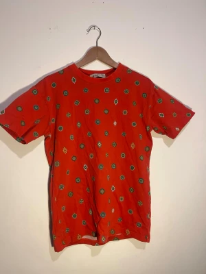 kenzo Röd mönstrad t-shirt med tryck - Kenzo Cool röd t-shirt med korta ärmar och färgglatt geometriskt mönster i grönt, blått och vitt. Skön passform och rund halsringning, perfekt för dig som vill sticka ut lite extra. Tillverkad i mjuk bomull för en bekväm känsla hela dagen.