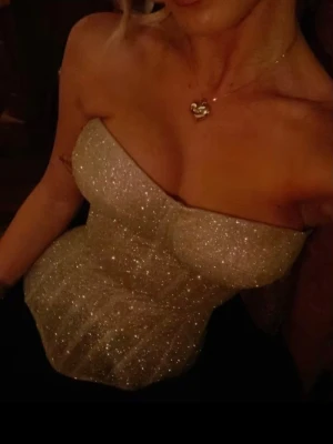 Glittrig guldfärgad korsettopp - Snygg axelbandslös korsett i guldfärgat, glittrigt material som ger en lyxig och festlig look. Formpressade kupor och markerad midja för en smickrande siluett. Perfekt att styla med kjol eller byxor för en trendig outfit. Justerbar i ryggen.