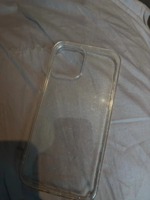 Transparent glittrigt mobilskal IPhone 12 Pro Max - Säljer ett genomskinligt mobilskal med glittereffekt. Skalets material är mjuk plast som ger bra grepp och skydd. Passar till mobil med större kameralins. Perfekt för dig som vill visa upp mobilen men ändå ha lite extra bling.