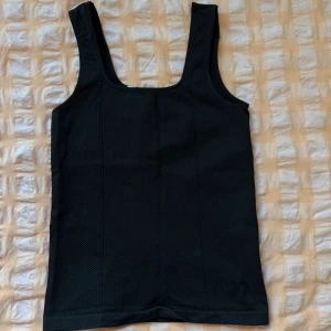 Svart linnetopp - Linnetopp med breda axelband och diskret logga nere vid fållen. Tillverkad i ett lätt och ventilerande syntetmaterial som passar perfekt till träning eller varma dagar. Enkel och stilren design med rak passform🦋