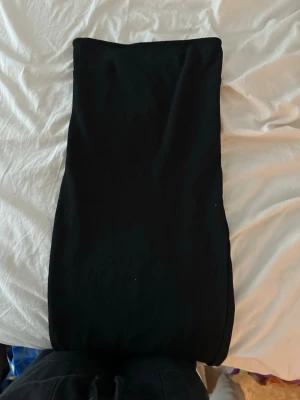 Svart långklänning i bomull - En enkel och stilren svart långklänning i mjukt bomullsmaterial. Klänningen har en rak passform och är helt utan mönster eller detaljer, vilket gör den lätt att styla med accessoarer. Perfekt för dig som gillar minimalistisk stil.