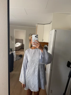 Ljusblå blommig klänning med vida ärmar - Säljer en jättefin ljusblå kort sommarklänning med blommigt mönster och vida, långa ärmar🩵