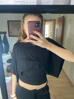 Svart croppad topp med vida ärmar - Säljer en svart croppad topp med vida, korta ärmar och lös passform. Toppen har en enkel och stilren look som passar perfekt till höga byxor eller kjol. Tillverkad i mjuk bomull för en skön känsla.