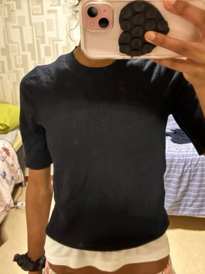 Svart ribbad croppad topp - En svart, ribbad croppad topp med korta ärmar och rund hals. Enkel och stilren design som passar till många olika outfits. Perfekt för dig som gillar en clean och modern look.