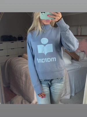 Ljusblå sweatshirt med tryck - Ljusblå sweatshirt med stort vitt tryck och texten 'maranr' på framsidan. Tröjan har rund halsringning, ribbade muddar vid ärmslut och nederkant samt en avslappnad passform. Perfekt för en chill och casual stil.