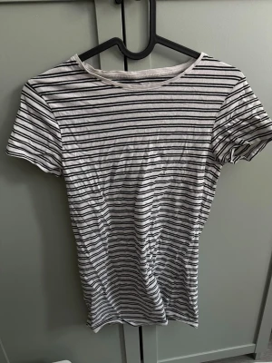 Vit och svart randig t-shirt - En klassisk vit t-shirt med svarta horisontella ränder. T-shirten har rund halsringning och korta ärmar. Tillverkad i mjuk bomull som känns skön mot huden. Perfekt basplagg för alla tillfällen och enkel att matcha med olika stilar. Tight modell. Från primark