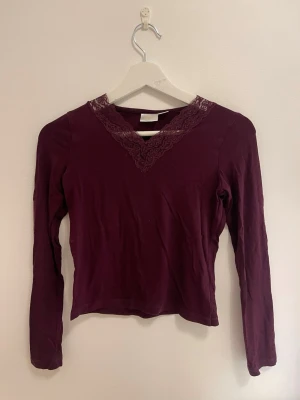 Vinröd topp med spetsdetalj - Vinröd långärmad topp med v-ringning och dekorativ spets runt halsen. Tunn och mjuk, perfekt för lager på lager eller som den är. Enkel men ändå elegant design som passar till mycket.