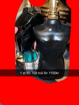 Jean Paul Gaultier Le Male parfym - Två flaskor Jean Paul Gaultier Le Male parfym i den ikoniska bystformade flaskan. En flaska är svart med guldigt lock och den andra har en mix av svart och turkost glas. Båda har en elegant och modern design som sticker ut i badrumshyllan.