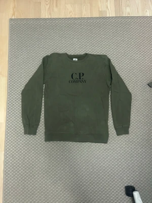 Sweatshirt från C.P. Company - Snygg grön sweatshirt från C.P. Company med rund halsringning och svart logotyp på bröstet. Tröjan har långa ärmar, ribbade muddar.  Passar s-m 