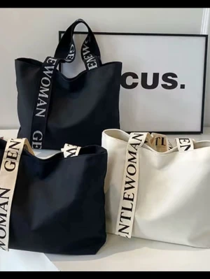 Shoppingväska med text Gentlewoman - Trendig shoppingväska i svart eller vit canvas med breda axelband där det står 'Gentlewoman'. Väskan har en enkel, rymlig design och passar perfekt för att bära allt du behöver under dagen. Snygg och praktisk för dig som gillar stilrena accessoarer.