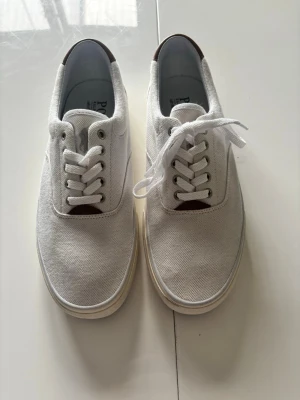 Nya vita canvas sneakers från Polo Ralph Lauren - Stilrena oanvända vita sneakers från Polo Ralph Lauren i canvasmaterial. Klassisk låg modell med vita snören och metallöljetter. Diskret logga broderad på plösen. Polo’s egna RLite cushioning i sulan. 