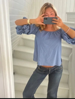 Ljusblå offshoulder blus med volangärm Zara  - Supersöt ljusblå blus med offshoulder-modell och vida volangärmar. Blusen har en lös passform och är tillverkad i ett mjukt bomullstyg som känns luftigt och skönt. Perfekt att styla med jeans eller kjol för en trendig look.