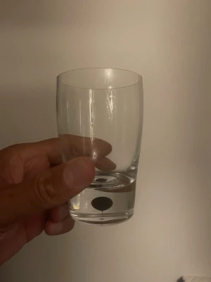 Genomskinligt glas med svart prick - Säljer ett stilrent, genomskinligt dricksglas i glas med en svart prick och en tunn linje nära botten. Glaset har en enkel, rund form och passar perfekt för vatten eller juice.