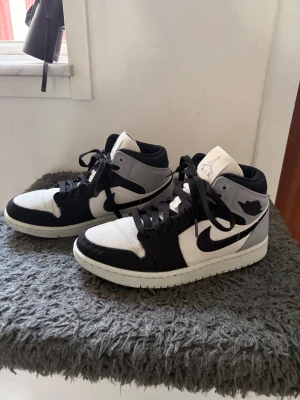 Air Jordan 1 Mid svart/vit/grå - Säljer ett par Air Jordan 1 Mid sneakers i svart, vitt och grått. Svarta skosnören och detaljer i mocka och läder. Ikonisk Jordan-logga på sidan och vadderad krage för extra komfort. Skorna är i mycket bra skick! 