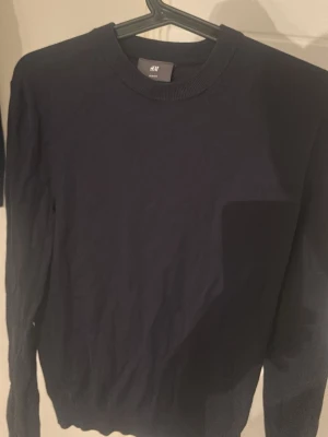 Mörkblå stickad tröja från H&M - En enkel och stilren mörkblå stickad tröja från H&M. Tröjan har rund halsringning och långa ärmar. Perfekt att matcha med jeans eller kjol för en clean look.