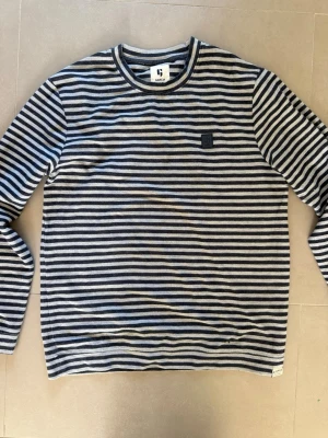 Randig stickad tröja från Garcia - Snygg stickad tröja från Garcia i marinblått och grått med horisontella ränder. Tröjan har rund halsringning och en diskret logga på bröstet. Perfekt för dig som gillar klassisk men avslappnad stil.